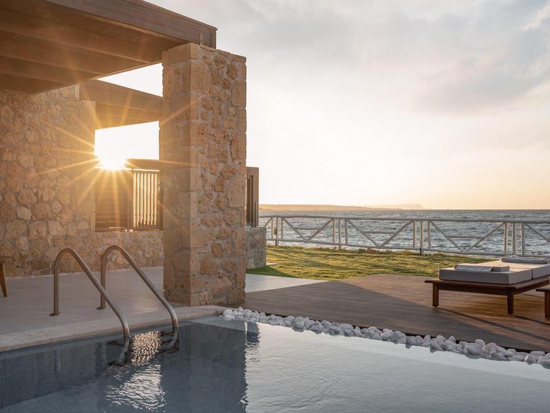 Área moderna de piscina con tumbonas y vista al mar al atardecer.