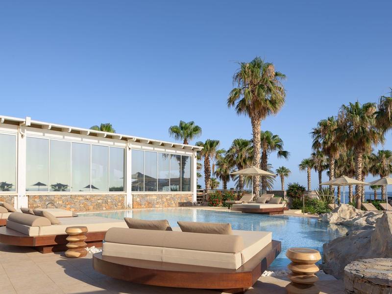 Área de piscina lujosa con tumbonas y palmeras bajo un cielo azul despejado.