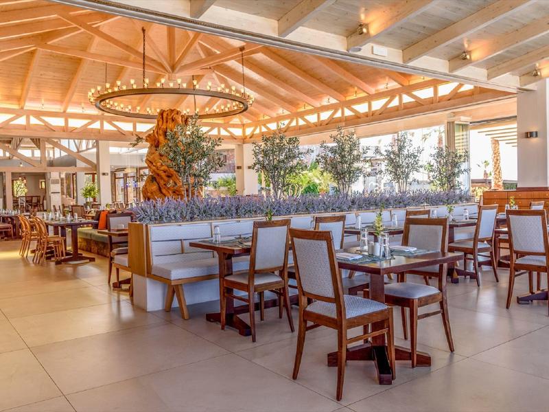 Restaurante de hotel luminoso con muebles de madera y decoración natural bajo un techo de vigas de madera.
