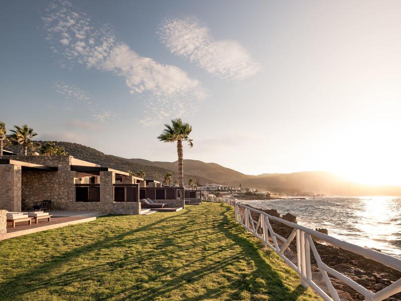 Hotel junto al mar con césped, paseo y palmeras al atardecer.