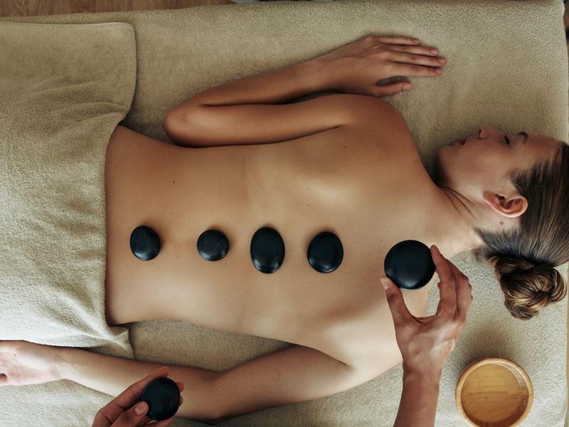 Mujer recostada con piedras calientes sobre la espalda en un tratamiento de spa relajante.