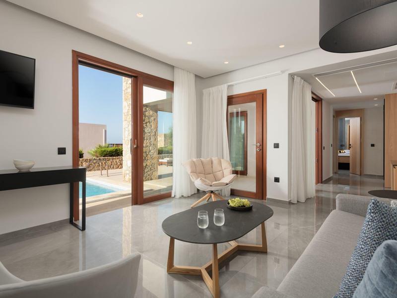 Sala moderna con acceso a la piscina, sofá, mesa de centro y grandes ventanales en un hotel.