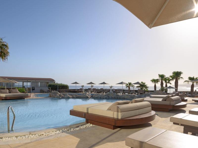 Área de piscina de lujo con tumbonas y sombrillas bajo cielo despejado junto al mar.