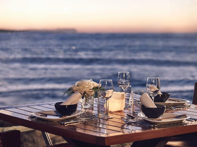Mesa elegante puesta junto al mar al atardecer, lista para una cena romántica.