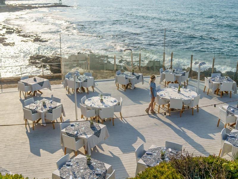 Terraza con varias mesas preparadas junto al mar en un hotel.