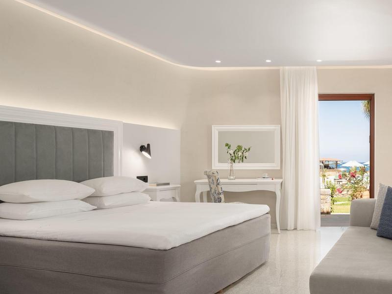 Habitación de hotel luminosa con cama grande, escritorio y vista al mar.