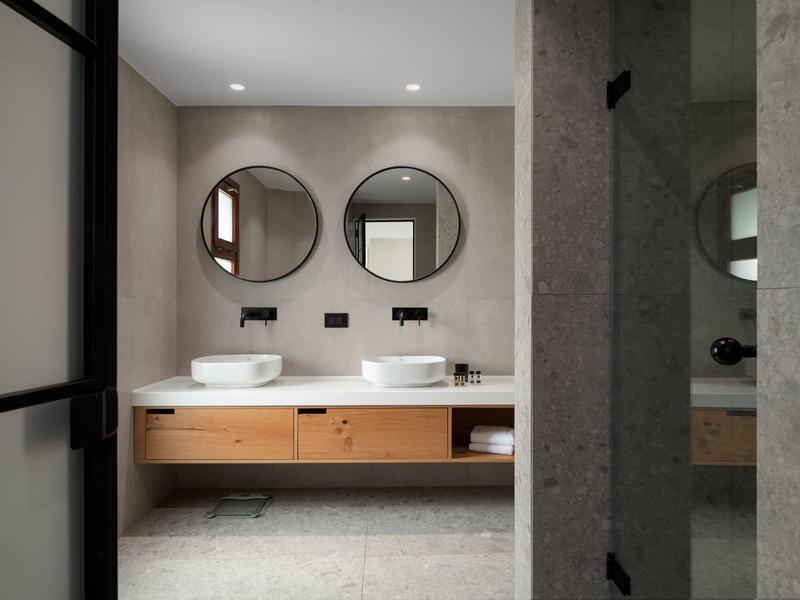 Baño moderno con dos espejos redondos y lavabos sobre un mueble de madera.