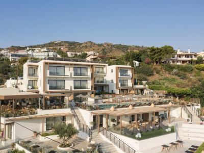 Modern multi-level hotel with terraces and pool, nestled on a hillside with clear blue sky.
