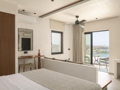 Bright hotel room with bed, desk, ceiling fan, and a balcony overlooking water.