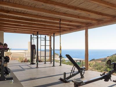 Open fitnessruimte met houten plafond en uitzicht op zee en kustlijn.