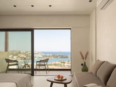 Modern hotel room with sea view, balcony seating, and neutral decor.