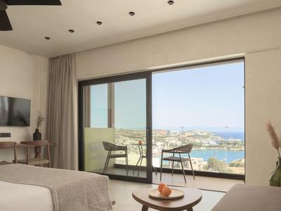 Modern hotel room with bed, TV, sliding glass door opening to balcony with sea view.