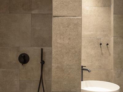Modern beige tiled bathroom with round white sink, black faucet, and black shower fixtures.