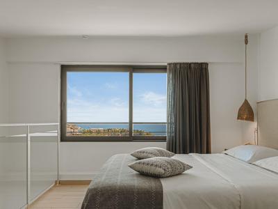 Bright bedroom with large window overlooking the sea, double bed, and minimalist decor.