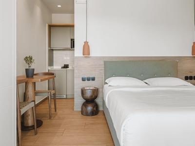 Minimalist hotel room with double bed, wooden floor, and small kitchen elements.