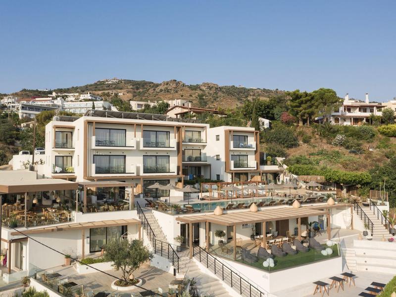 Modern multi-level hotel with terraces and pool, nestled on a hillside with clear blue sky.