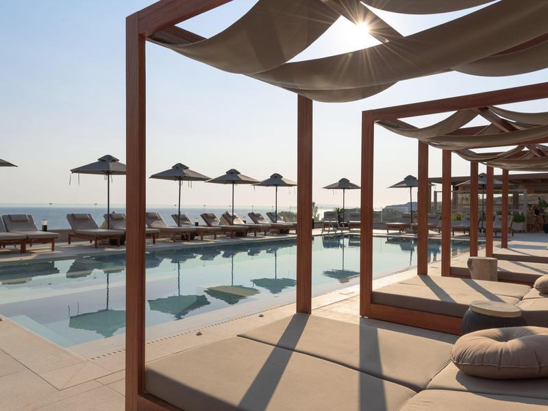 Poolside luxury beds and umbrellas overlooking the sea at sunrise.