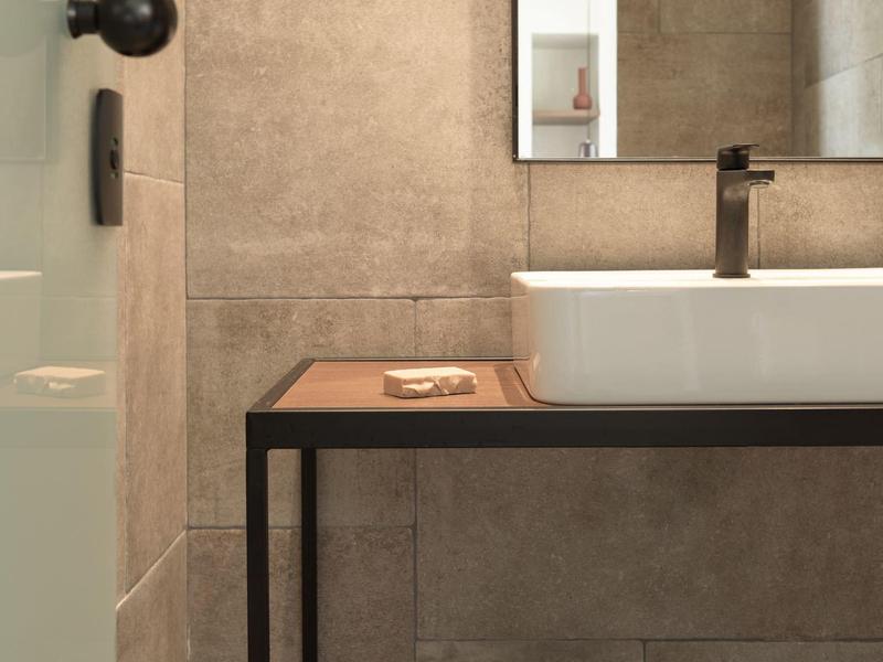 Modern bathroom with beige tiles, black faucet, rectangular mirror, and white sink on a black metal table.