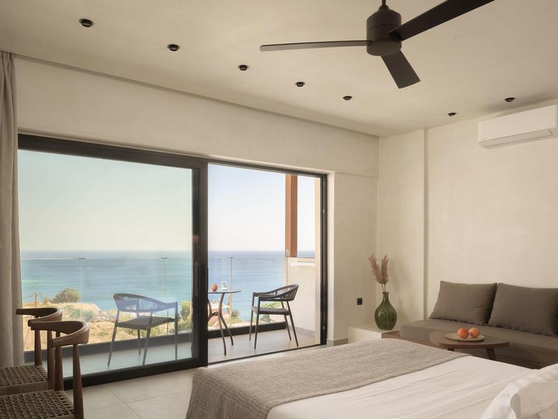 Room with sea view, bed, sofa, and balcony with chairs and table