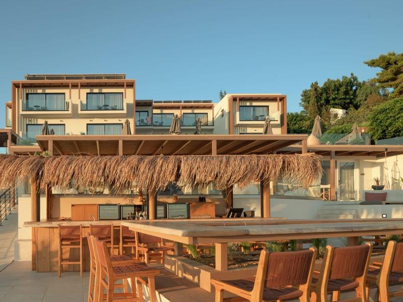 Outdoor seating area with wooden tables and chairs under a thatched roof near a hotel building.
