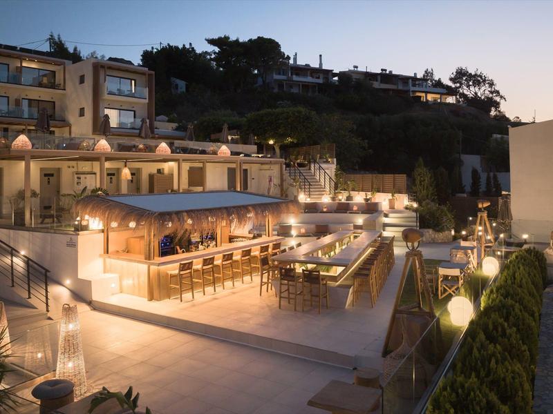 Elegant outdoor hotel bar and seating area lit up in the evening against hillside.