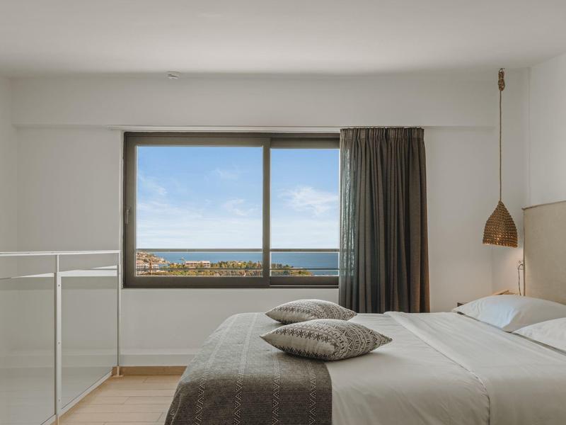 Bright bedroom with large window overlooking the sea, double bed, and minimalist decor.