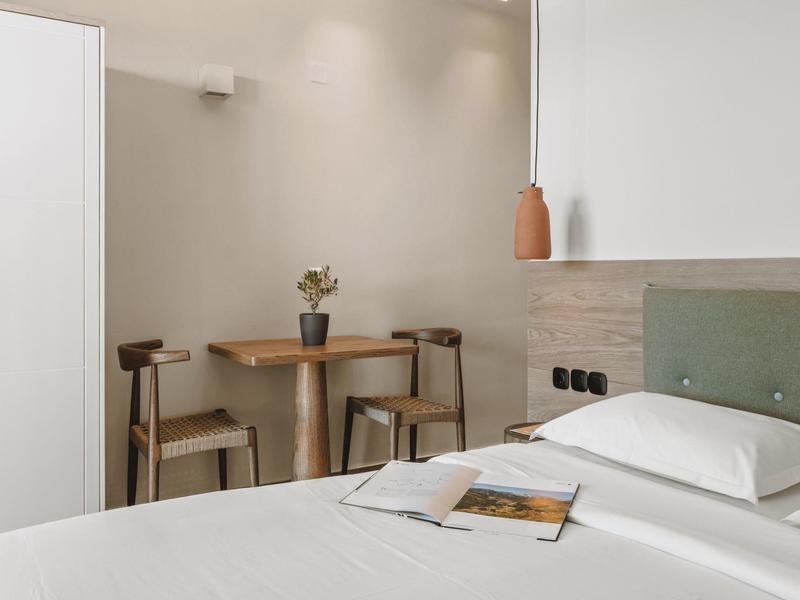 Modern, simply furnished hotel room with bed, nightstand, and dining area.