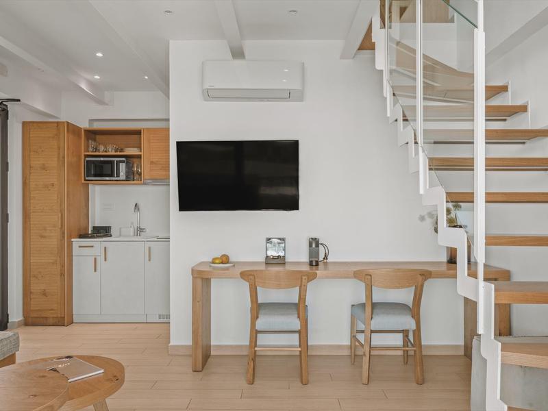 Modern living room with stairs, TV, table, and two chairs in neutral tones.