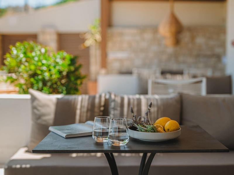 Cozy outdoor seating with cushions, table with glasses, a book, and a bowl of fruit.