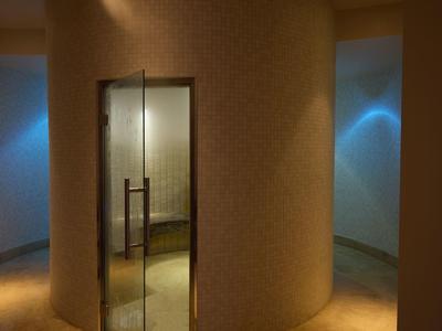 Moderní hotelová chodba se zakřivenou strukturální stěnou a skleněnými dveřmi za tlumeného osvětlení.