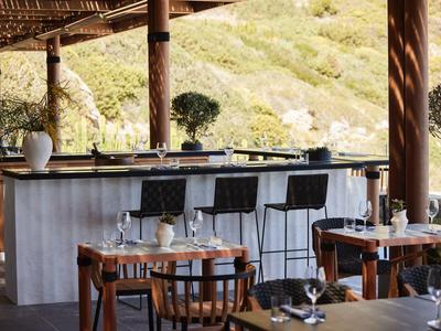 Moderní venkovní bar s dřevěným nábytkem a židlemi před zelenými kopci