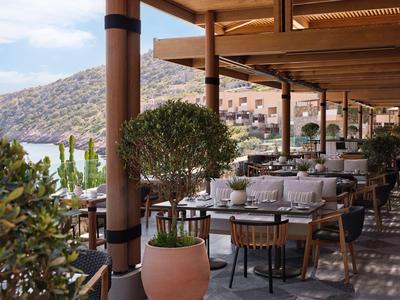 Offene Terrasse mit gedeckten Tischen und Blick auf Hügel und Wasser