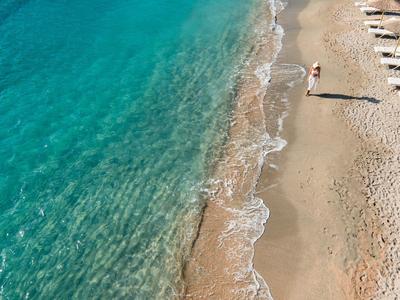 Čistá modrá voda se setkává s písčitou pláží s roztroušenými lehátky a jednou osobou.