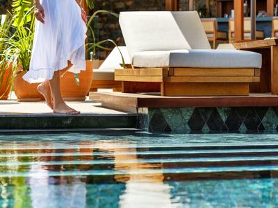 Osoba v bílém županu kráčí vedle bazénu vedle pohodlného lehátka.