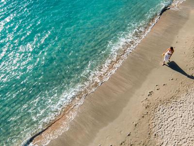 Eine Person läuft allein am ruhigen Strand entlang des klaren türkisfarbenen Wassers.