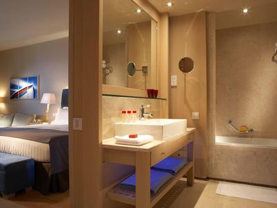 Moderní hotelová koupelna s umyvadlem a vanou, sousedící s ložnicí.