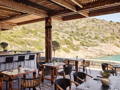 Offenes Restaurant mit Holzmöbeln und Blick auf Hügel und Meer.