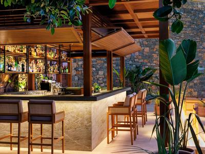 Ein moderner Hotelbarbereich mit Holztheke, Hockern und Pflanzen in warmer Beleuchtung.