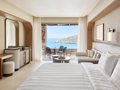 Modernes Hotelzimmer mit großem Bett, Sitzbereich und Meerblick durch eine breite Glasfront.