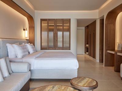 Modernes Hotelzimmer mit Doppelbett, Sofa, Holzdetails und warmem Licht.