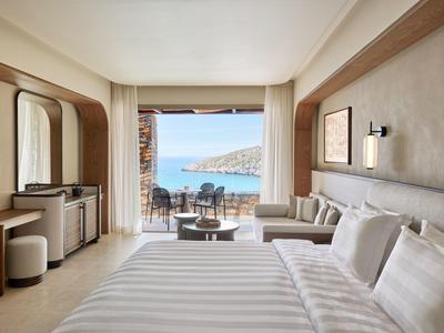 Moderní hotelový pokoj s velkou postelí a výhledem na terasu a moře.