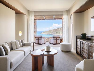 Jasný obývací pokoj s posezením a výhledem na moře a kopce přes velký otvor dveří.