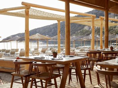 Světla restaurace s dřevěným nábytkem a výhledem na moře na slunečné pláži.