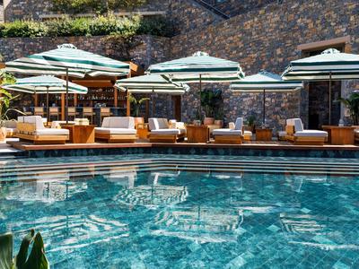 Luxuriöser Poolbereich mit Sonnenschirmen und Liegen vor einer Steinmauer im Hotel