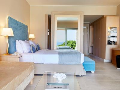 Hell eingerichtetes Hotelzimmer mit Doppelbett, Sitzbereich und Blick durch die Tür ins Grüne