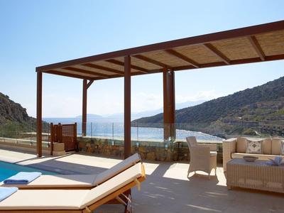 Terrasse mit Poolblick, Loungemöbeln und Bergkulisse bei klarem Himmel.