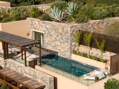 Moderner Pool mit Glasgeländer in einem Garten mit steinernen Wänden und Pflanzen.