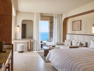 Helles Hotelzimmer mit Doppelbett, Sitzbereich und Blick auf das Meer durch große Fenster.