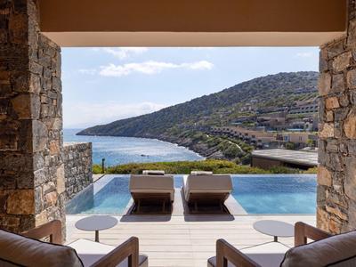 Blick auf einen Infinity-Pool mit zwei Liegestühlen und Meeresblick zwischen Steinmauern.