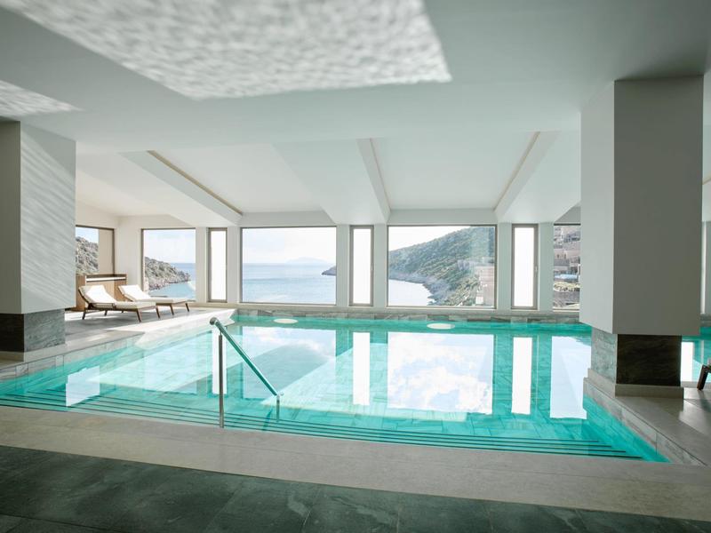 Vnitřní bazén s velkými okny a výhledem na moře v moderním hotelu.